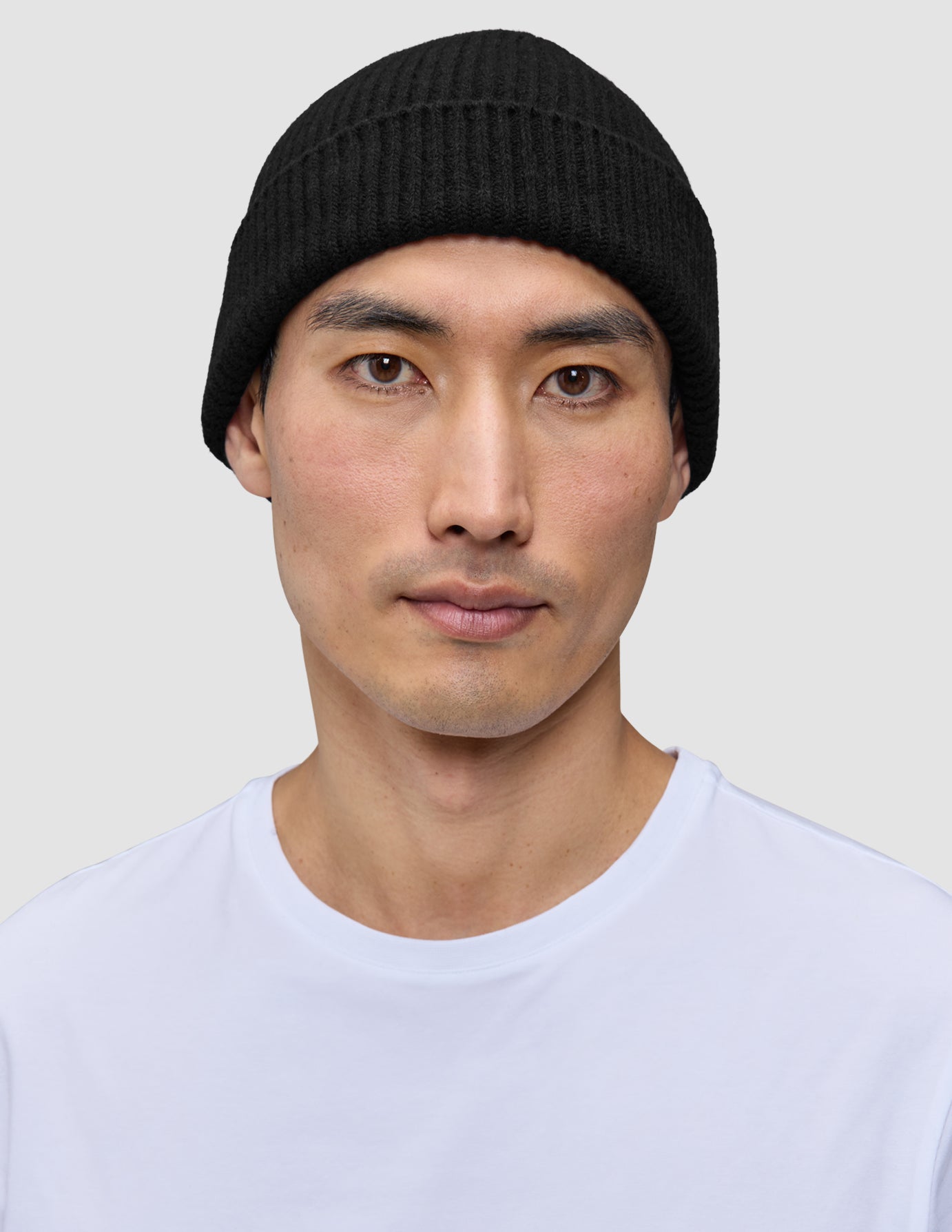En man som bär en svart, ribbad mössa i merinoull, modell Beanie Black.